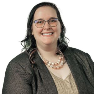 A person wearing glasses and a necklace, smiling in professional attire.