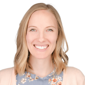 Smiling woman with blonde hair in floral top and light cardigan against white background.