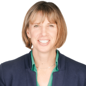 A smiling woman in a blue blazer and green shirt, against a white background.