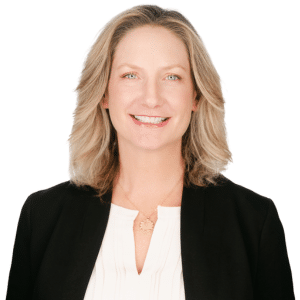 A woman smiling in a black blazer and white shirt against a white background.