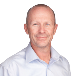 A man in a white collared shirt smiling against a white background.