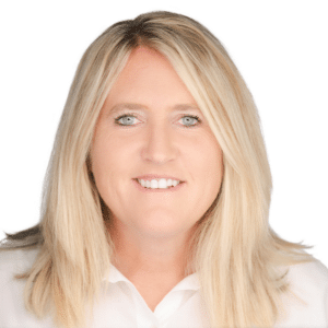 A woman smiling with long blonde hair in a white shirt against a plain background.
