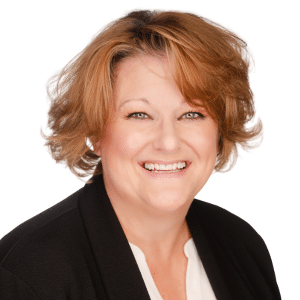 A woman with short, wavy hair smiling, wearing a black blazer and white shirt against a white background.