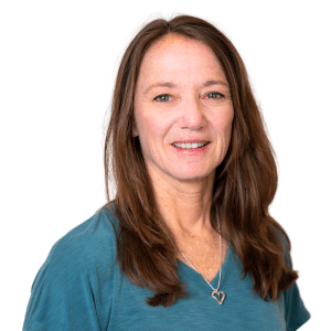 A woman smiling in a blue shirt with a heart necklace.