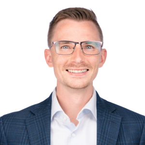 A smiling man in a blue suit wearing glasses with a white background.