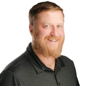 Man with a beard wearing a dark polo shirt, smiling against a white background.