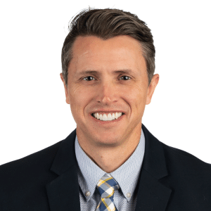 A smiling man in a suit and tie with a white background.