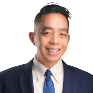 A man in a suit and tie smiling against a white background.