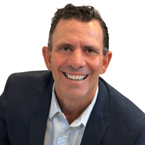 A smiling man in a suit and shirt against a white background.