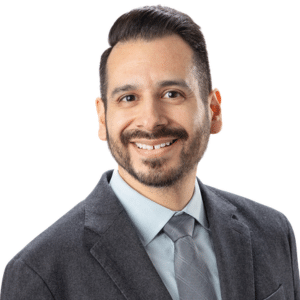 Man in a suit smiling with a neutral background.