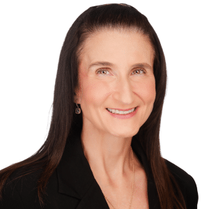 A woman in a black blazer smiling against a white background.