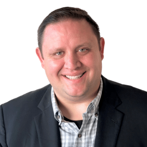 A man smiling at the camera, wearing a blazer and checked shirt against a white background.
