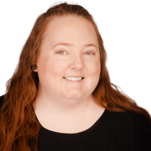 A woman with long red hair smiling, wearing a black top on a white background.