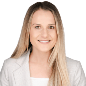 A woman smiling in a white blazer against a plain background.