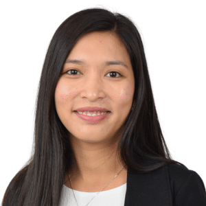 A woman with long dark hair smiling, wearing a business outfit against a white background.