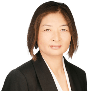 A woman in a black blazer and white blouse, smiling against a white background.
