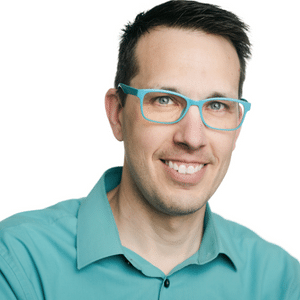 A man wearing turquoise glasses and a matching shirt smiles at the camera.
