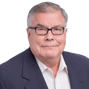 A man wearing glasses and a suit smiles for a portrait.