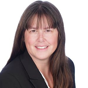 A woman with long brown hair wearing a black blazer smiles at the camera.