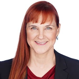 A person with long red hair and a business suit smiling in a professional portrait.