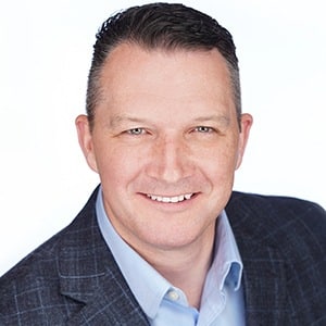 Man in business attire smiling against a plain background.