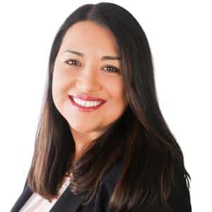 Smiling woman with long dark hair, wearing a black blazer, against a white background.