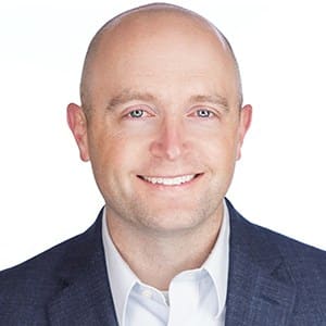 A person in a business suit smiling against a white background.