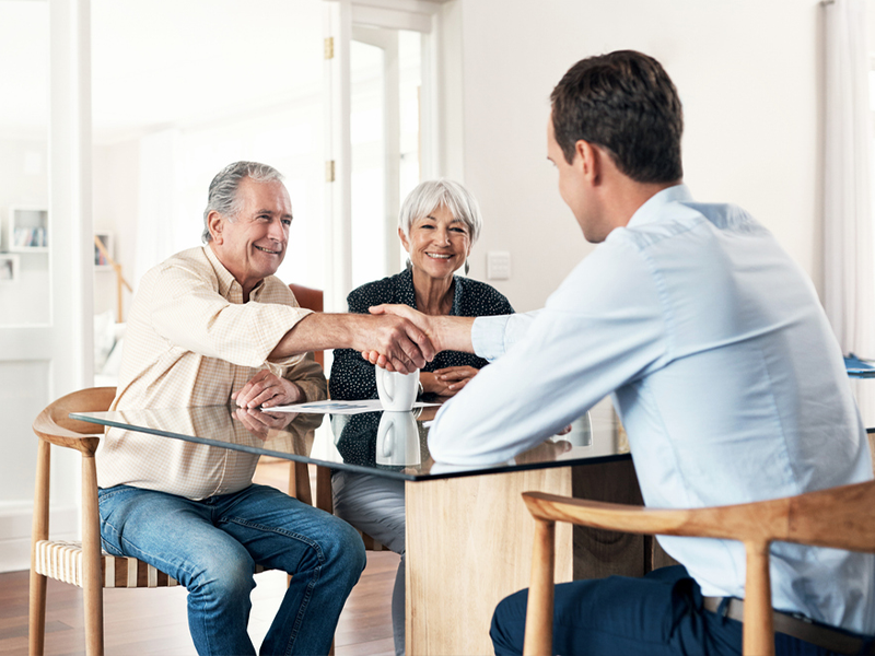 A couple shaking hands with a professional man while sitting at a table indoors.